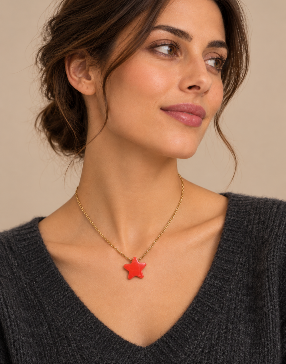 A woman wearing a gold chain necklace with a red star-shaped pendant, shown in a close-up portrait against a warm beige background.